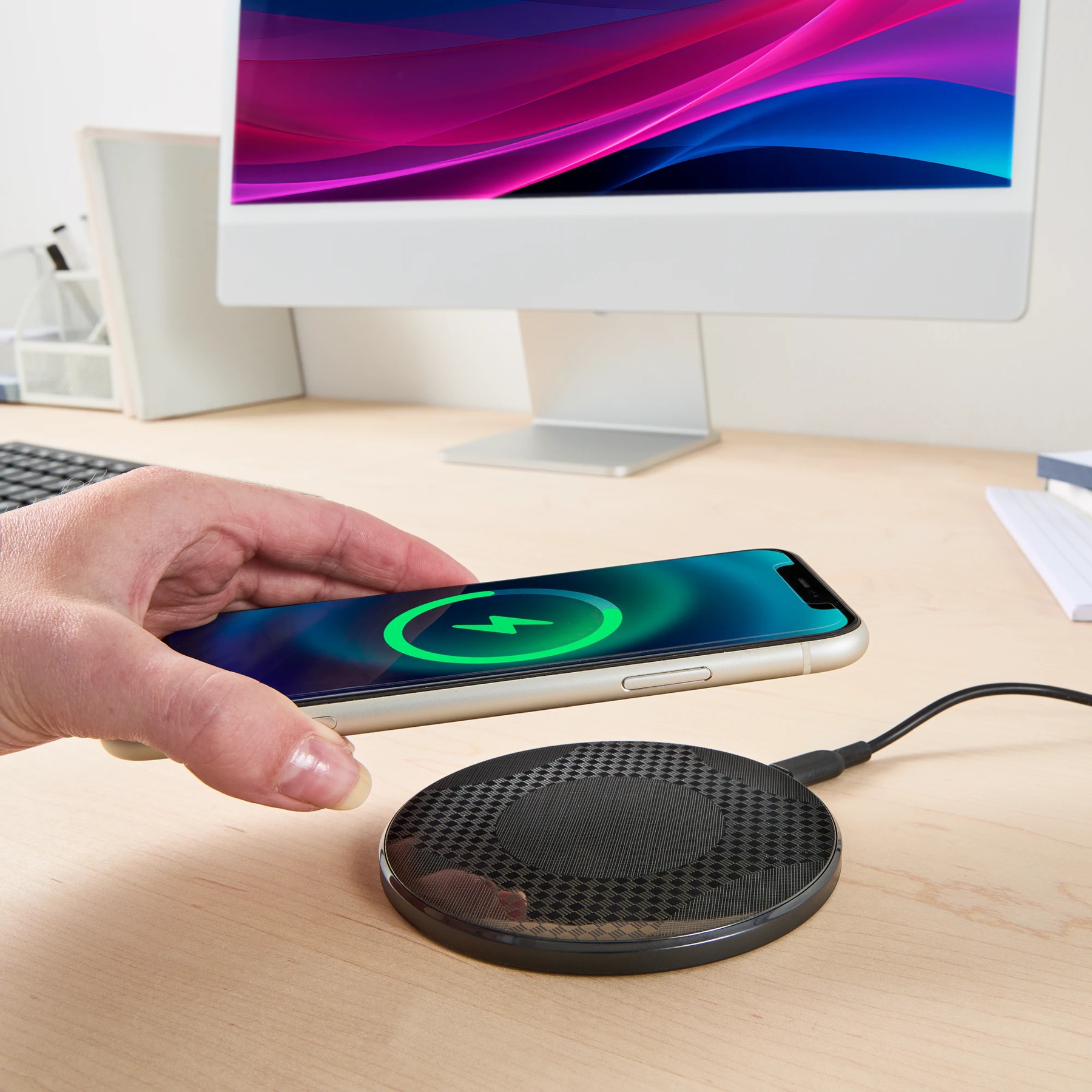Hand placing a smartphone onto a wireless charging pad on a clean office desk